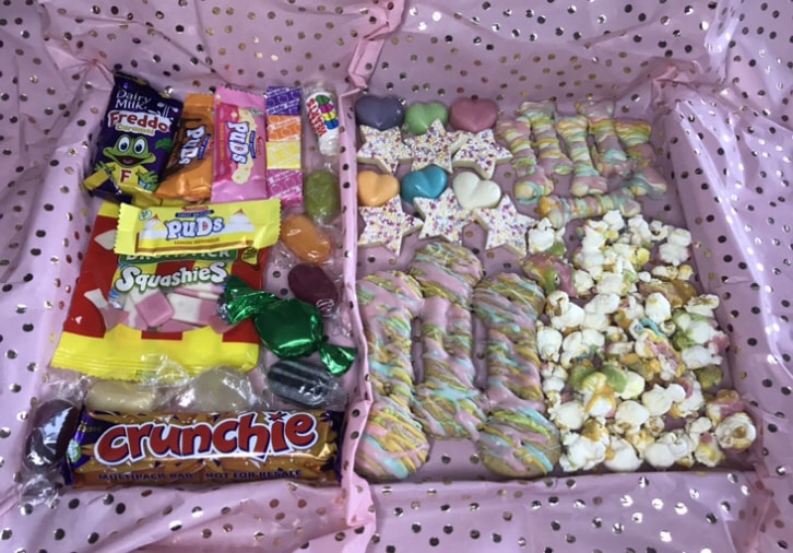 Picture shows a treat box filled with human goodies on the other side, such as Freddo chocolate, Crunchie bar, and other sweeties, with dog treats on the other side that are bone and star shaped with sprinkles.